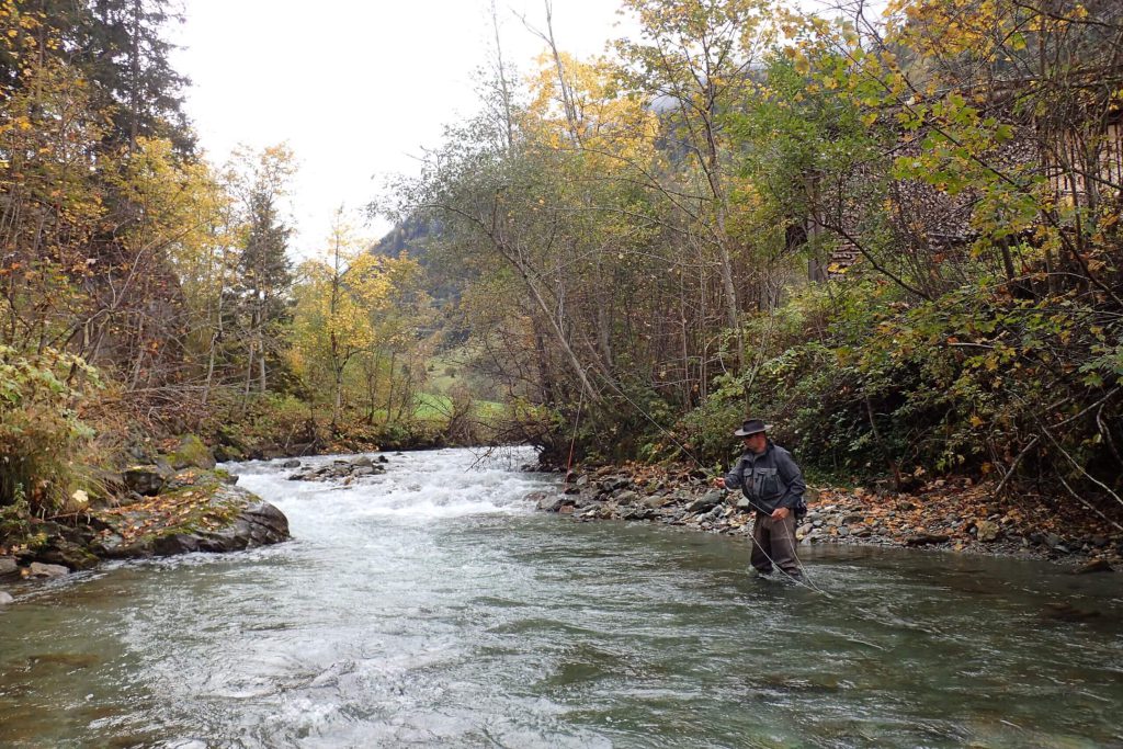 Fischer steht in einem klaren Fluss umgeben von herbstlichen Bäumen im Nationalpark Hohe Tauern.