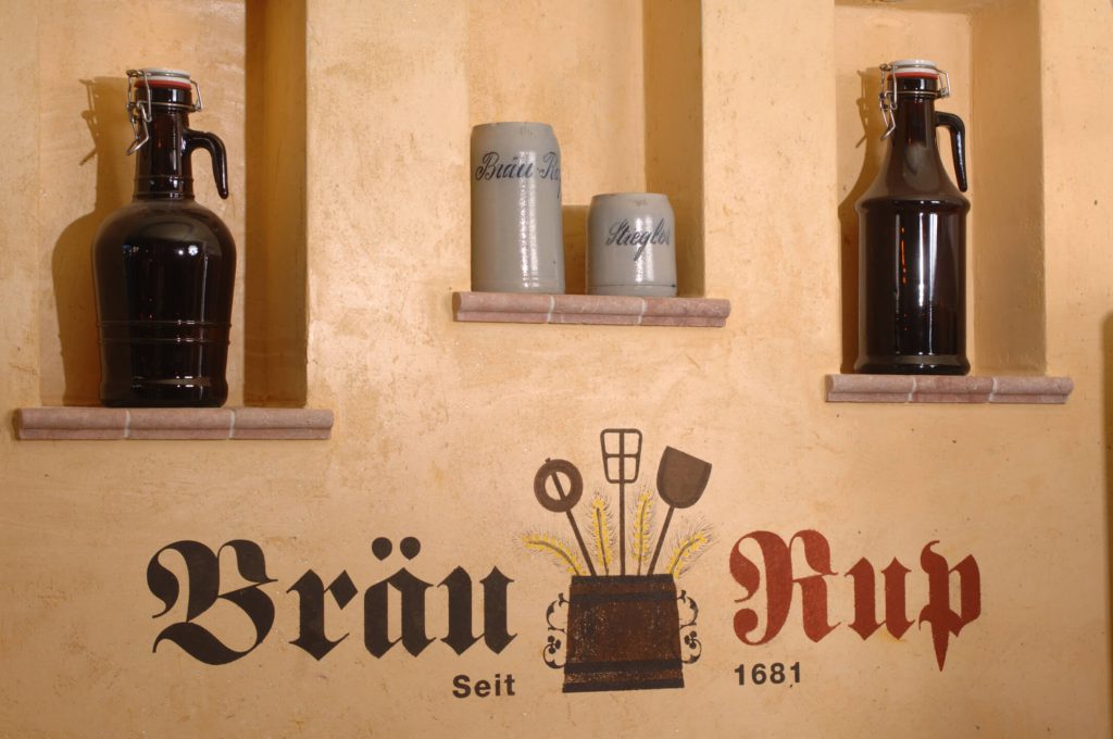 Brauerflaschen und eine Tonkanne dekorieren die Wand im Hotel Bräurup. Historisches Ambiente.